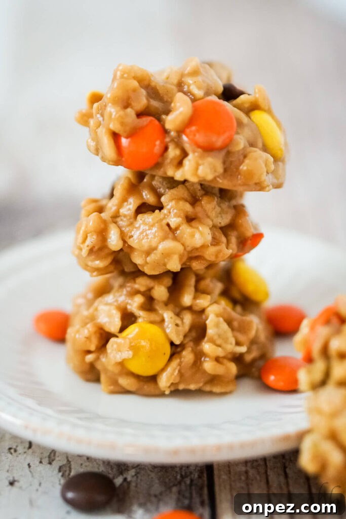 No-Bake Rice Krispies Cookies Recipe 3 A stack of 3 no bake rice krispies cookies with reeses pieces on a white plate.