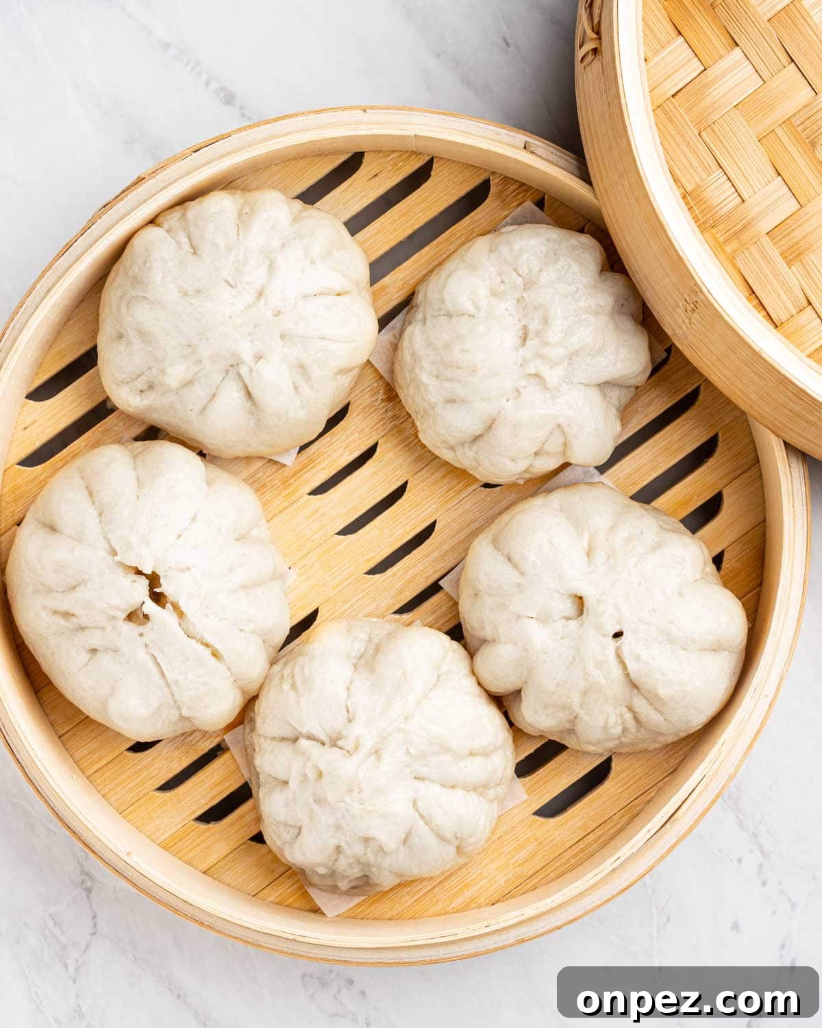 5 steamed buns on a bamboo steamer basket.
