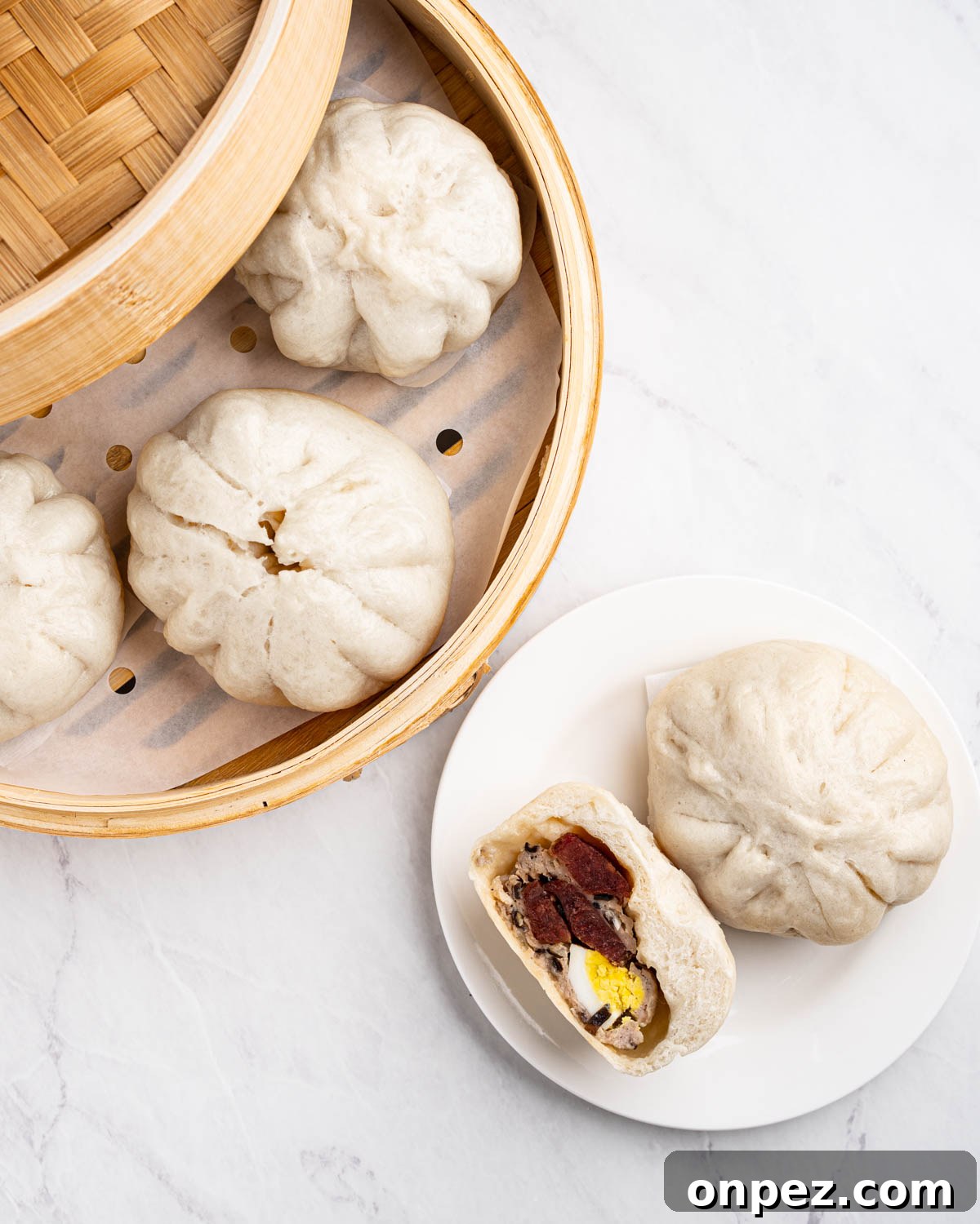 Steamer basket full of steamed buns with a plate of banh bao cut in half.
