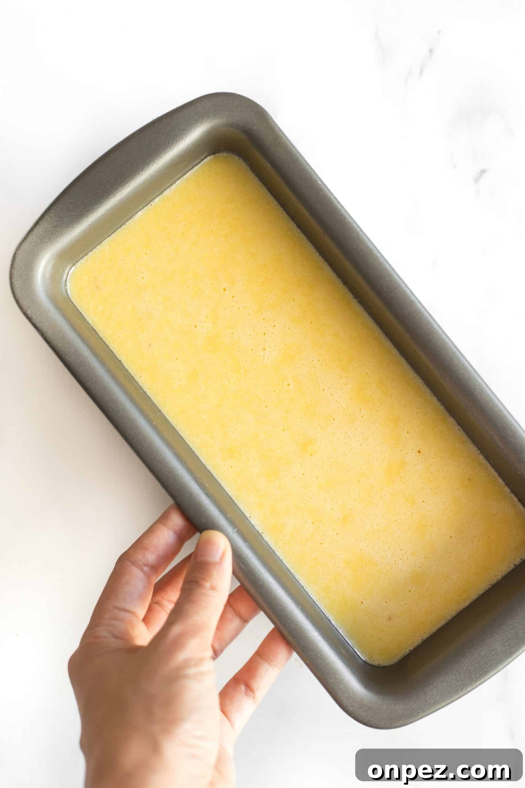 Holding a loaf pan with almond bread batter.