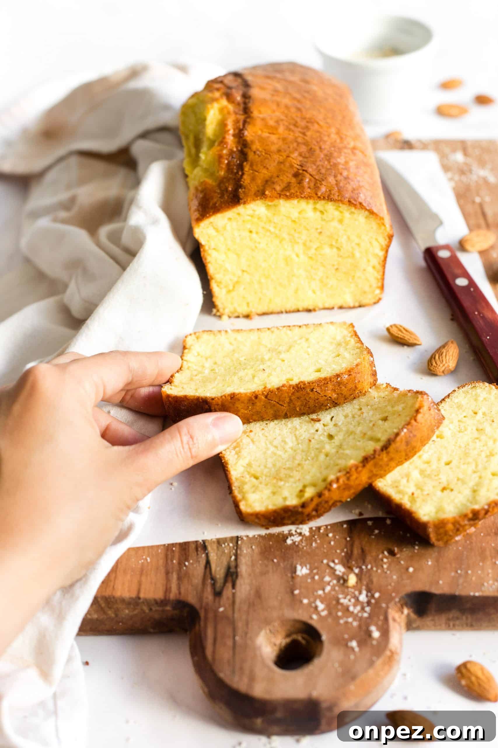 Reaching for a slice of low carb almond flour bread on a wooden board.