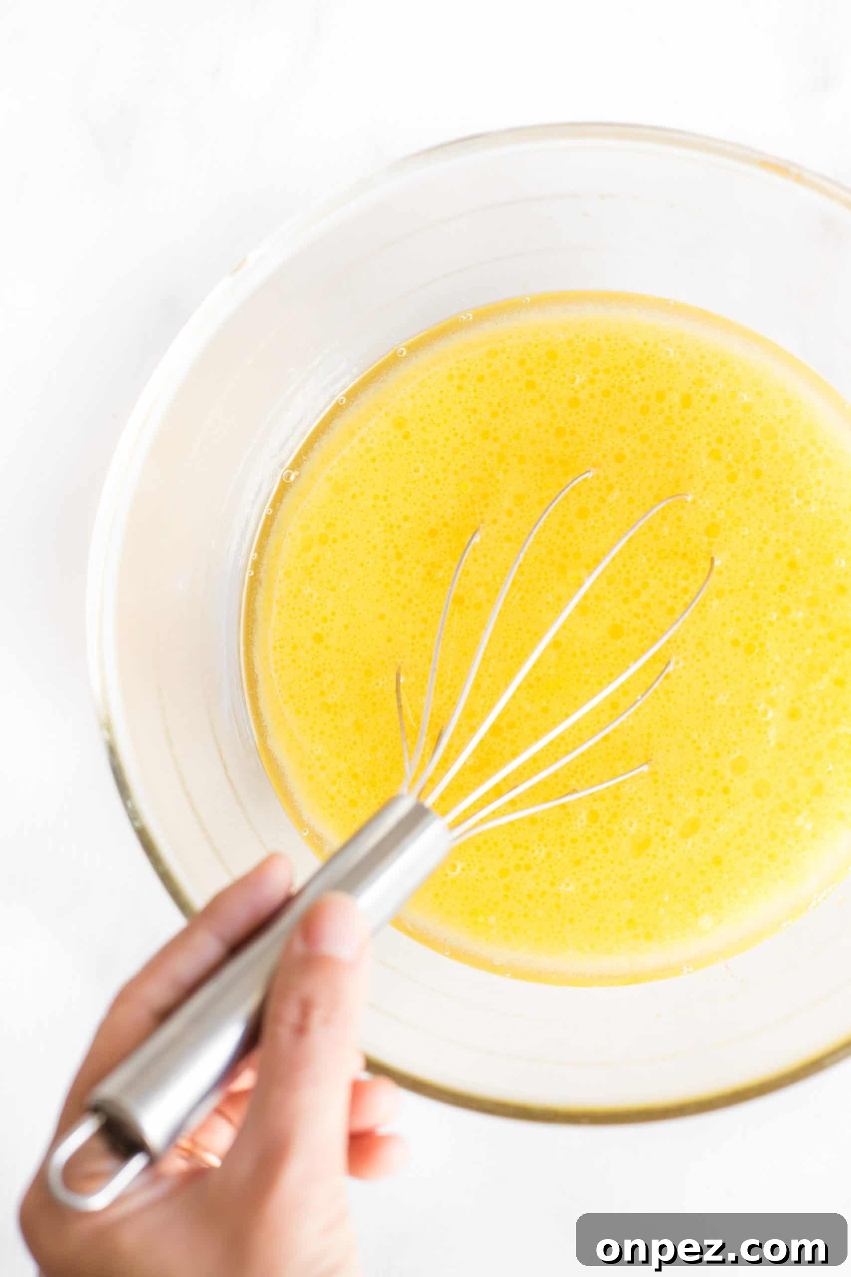 Whisking yellow mixture in a glass mixing bowl.