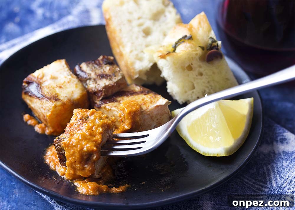 Grilled swordfish kebab topped with romesco sauce. A fork lifting a cube of grilled fish all covered with romesco sauce.