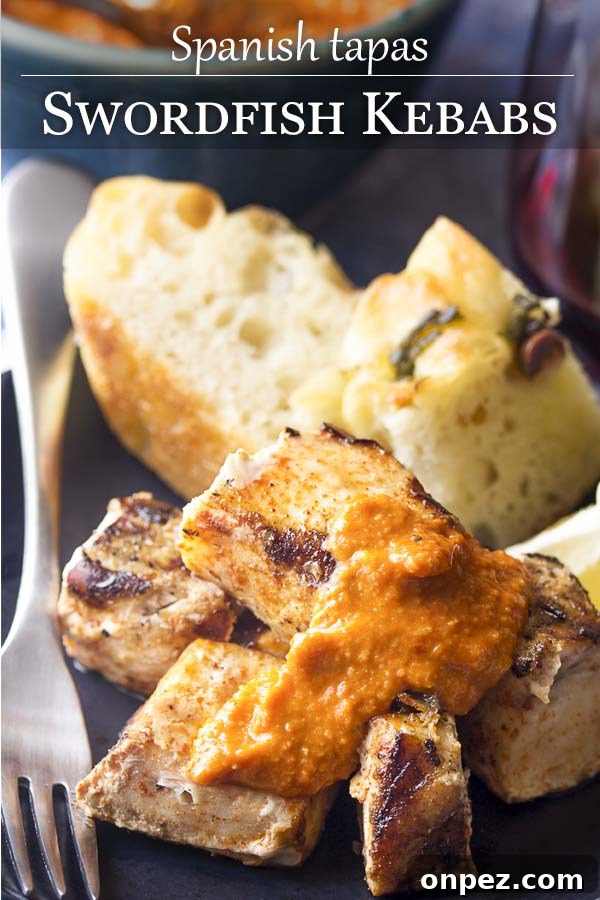 Cubed grilled fish on a plate with romesco sauce - Swordfish Kebabs. Cubed grilled fish on a plate with romesco sauce and text overlay - Swordfish Kebabs.