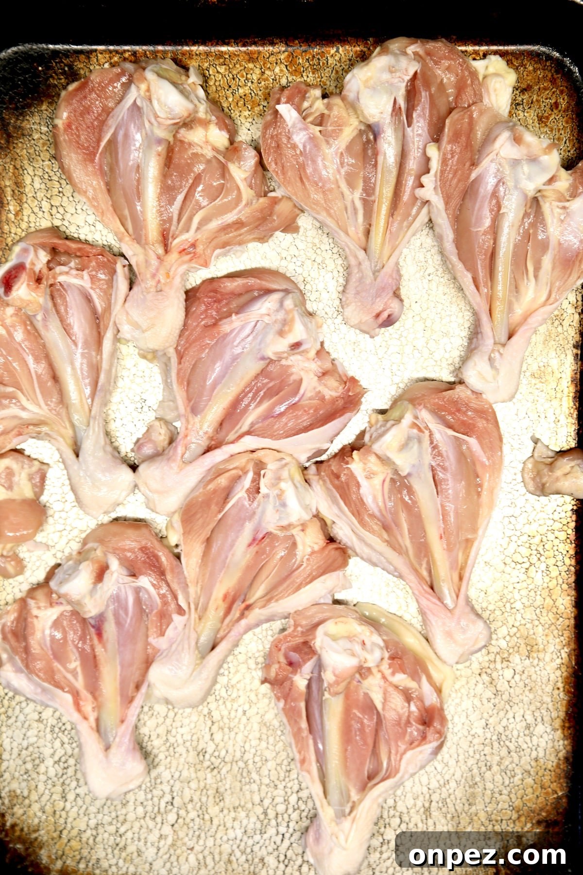Raw butterflied chicken legs on a sheet pan.