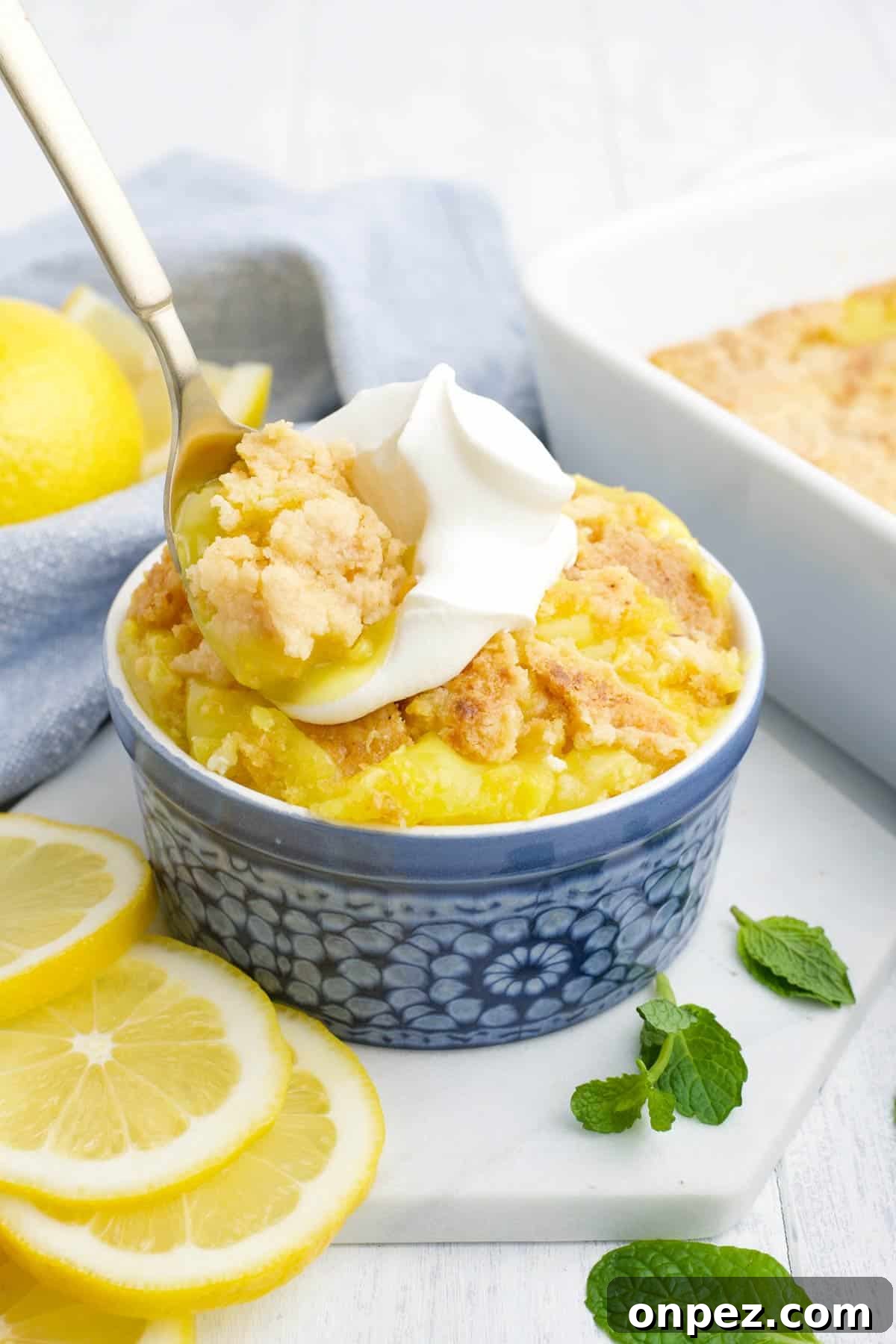 Quick Lemon Dump Cake Recipe 5 A spoon with a bite of lemon cake up over the bowl topped with whipped cream.