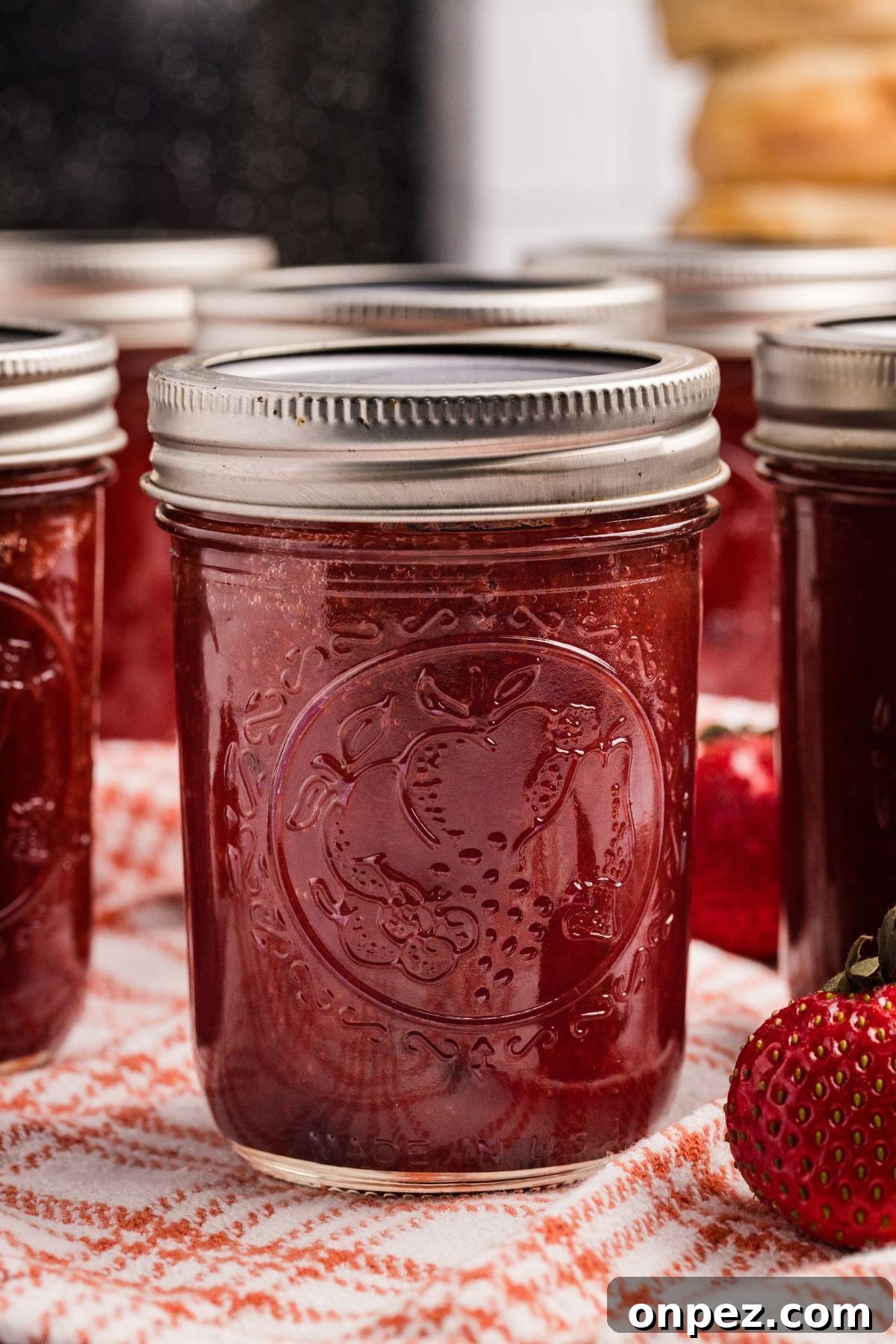 Homemade Strawberry Butter Canning Recipe and Tips 2 Close-up of a jar of strawberry butter with more jars and strawberries behind it.