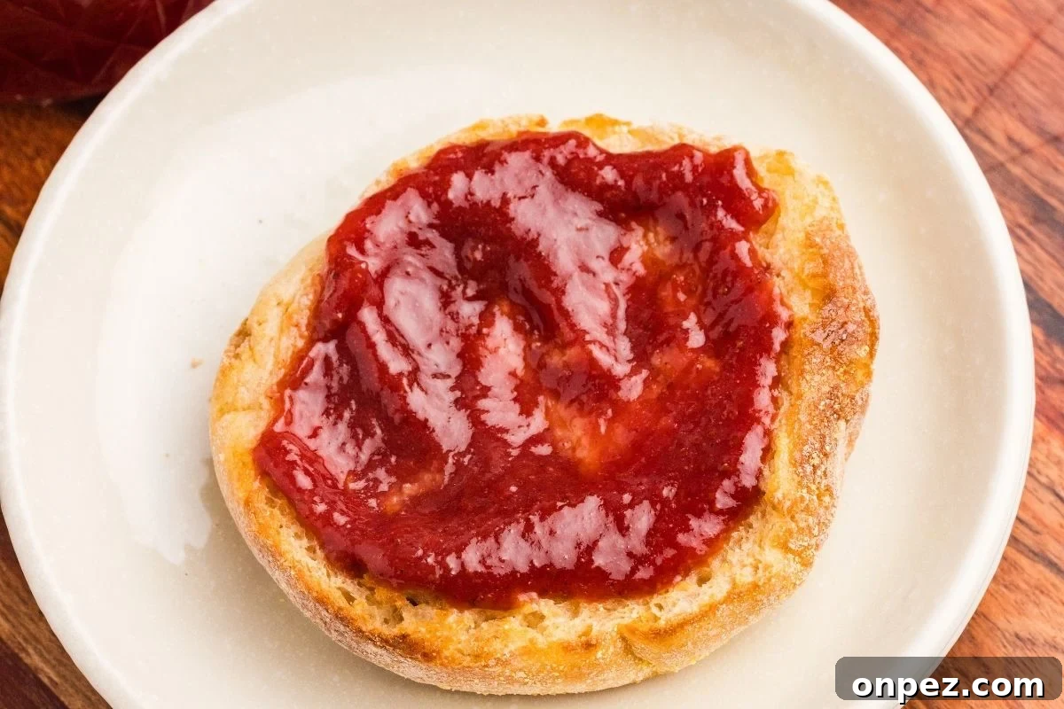 Homemade Strawberry Butter Canning Recipe and Tips 12 Strawberry butter spread on a toasted English muffin on a white plate.