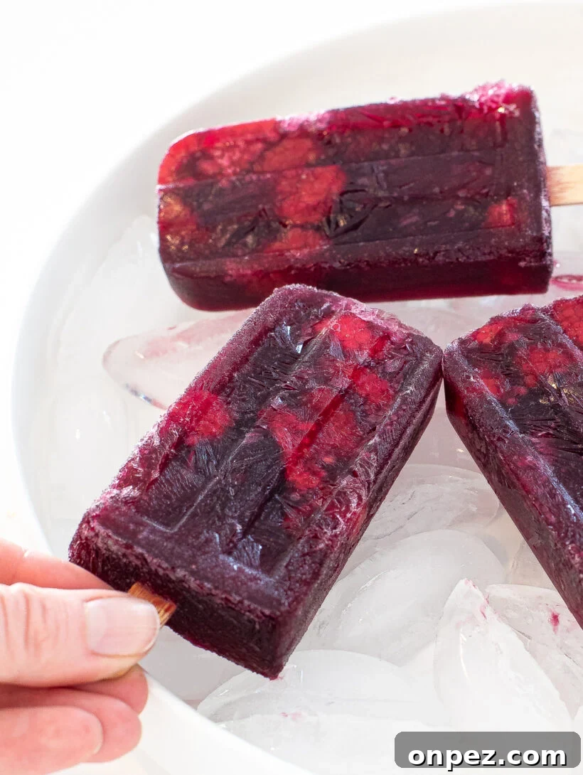 Sangria Popsicle Recipe: Refreshing Wine Pops for Summer 7 Popsicles on a bed of ice with one hand holding a popsicle.