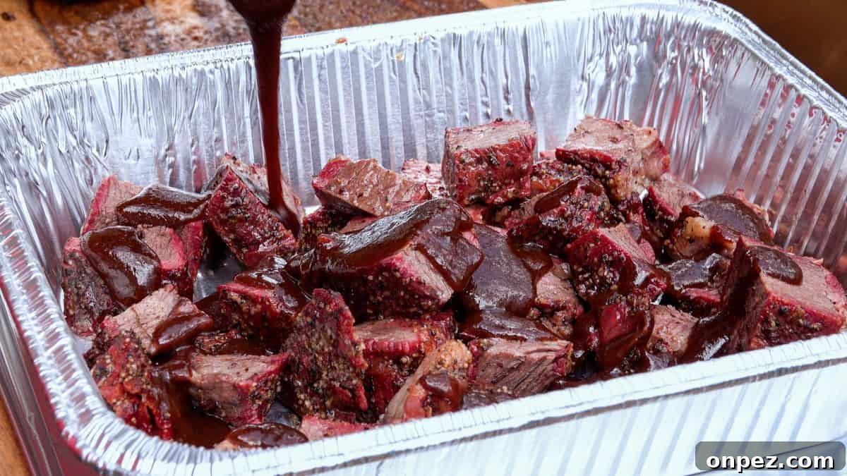 Budget Burnt Ends: Incredibly Tender Brisket Bites 8 Barbecue sauce being poured over smoked chuck roast in aluminum pan