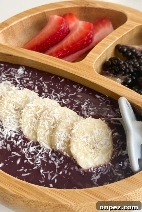 Acai bowl for kids served with sliced bananas, strawberries, blackberries and coconut.