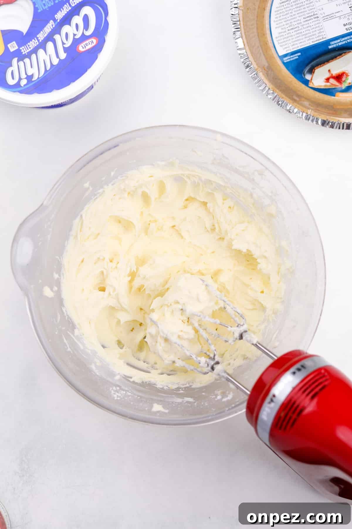 An electric mixer blending cream cheese with sugar.