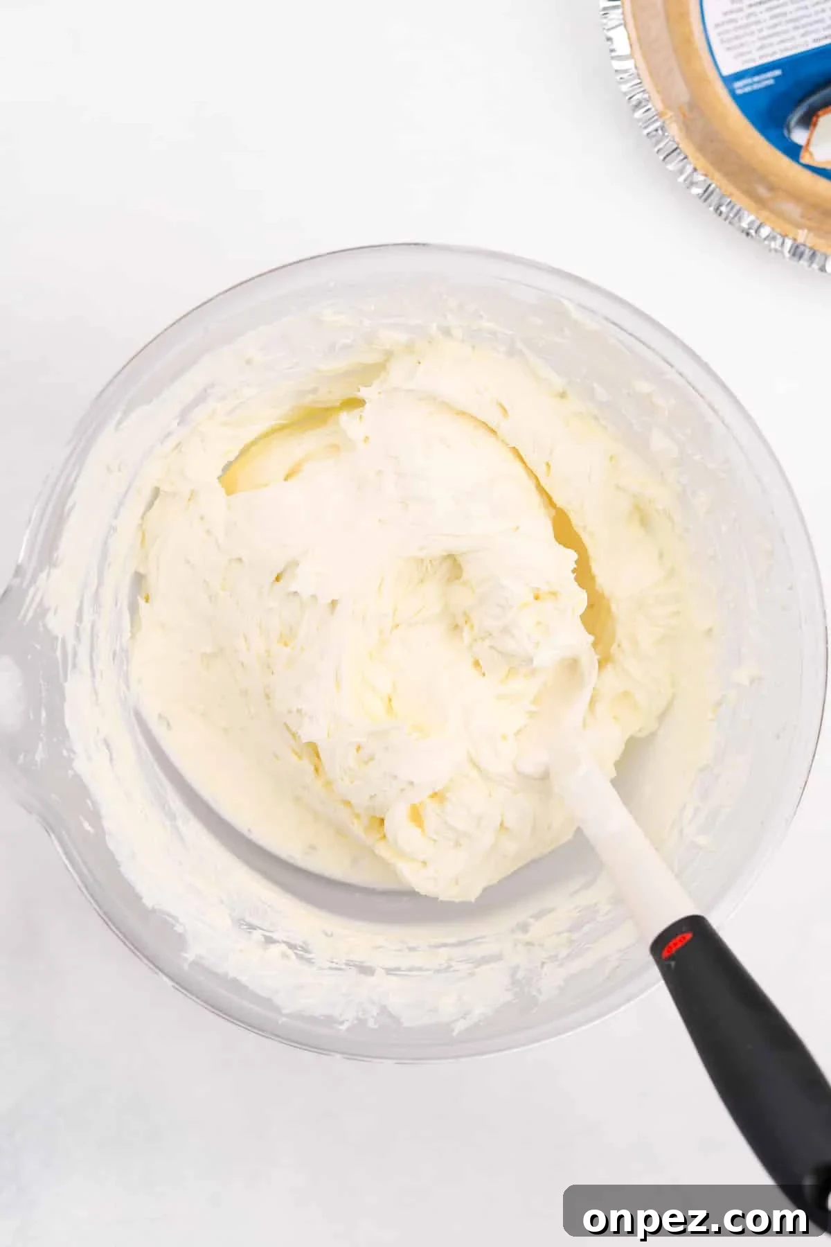 A rubber spatula stirring a bowl of cheesecake filling.