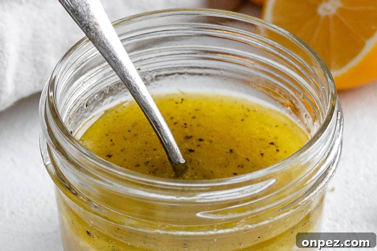 Bright Lemon Vinaigrette for Salads & Marinades 2 completed lemon dressing in a glass jar with a spoon in it and ingredients in the white background