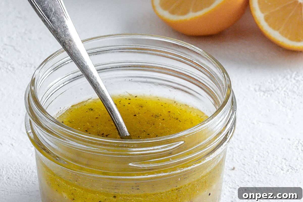 Bright Lemon Vinaigrette for Salads & Marinades 3 completed lemon dressing in a glass jar with a spoon in it and ingredients in the white background