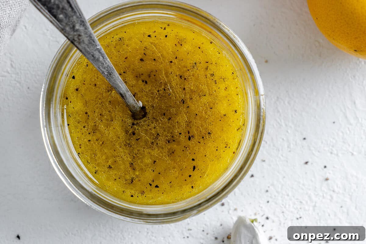 Bright Lemon Vinaigrette for Salads & Marinades 8 completed lemon dressing in a glass jar with a spoon in it and ingredients in the white background