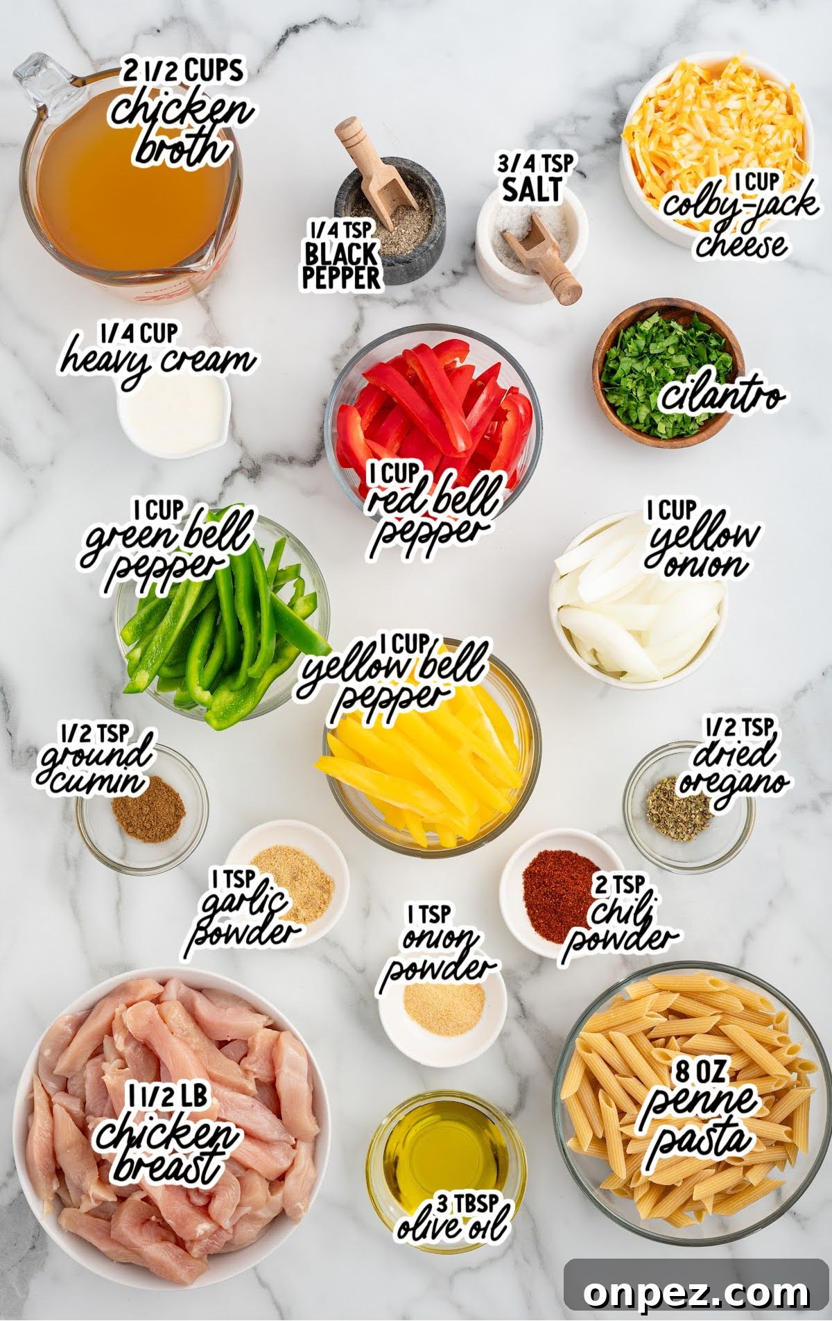 One-Pot Chicken Fajita Pasta Recipe 3 Overhead layout of all ingredients for chicken fajita pasta labeled with text. Ingredients include chicken breast, penne pasta, bell peppers, onion, garlic powder, chili powder, cumin, oregano, chicken broth, heavy cream, cheese, olive oil, and seasonings.