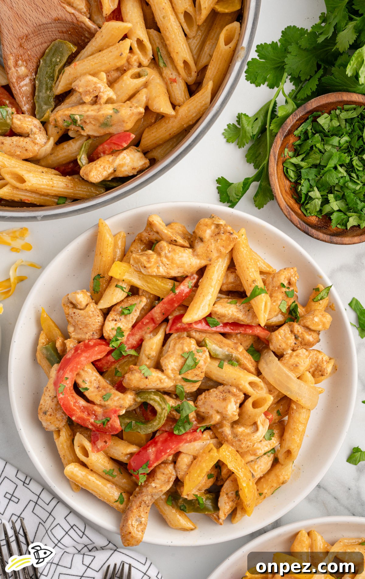 One-Pot Chicken Fajita Pasta Recipe 6 Overhead view of a bowl filled with chicken fajita pasta beside a pot of the same dish.