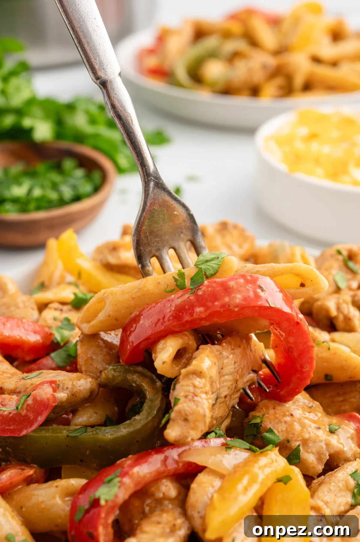 One-Pot Chicken Fajita Pasta Recipe 7 Close-up of a fork lifting a bite of creamy chicken fajita pasta with red and yellow bell peppers and chicken strips.