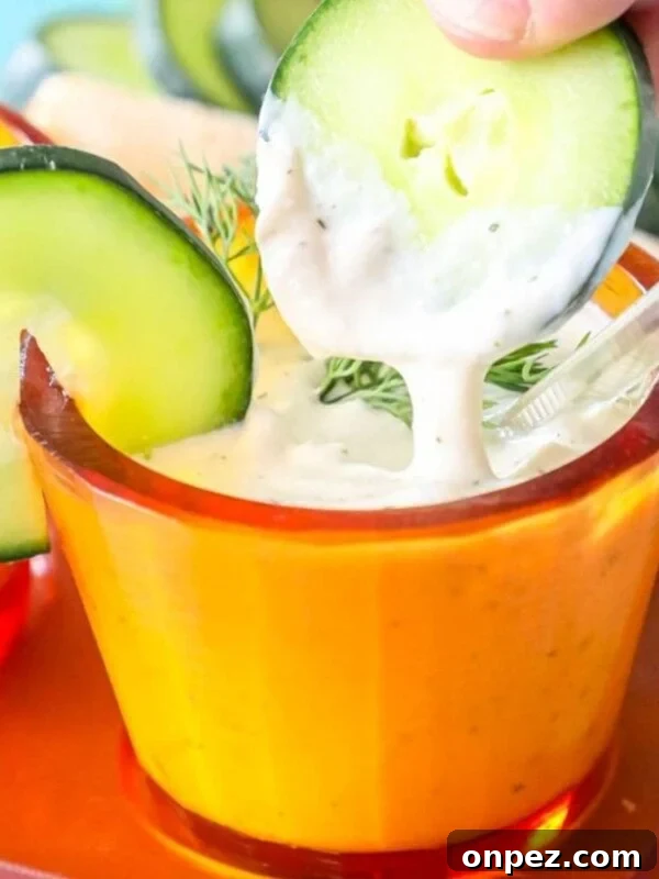 a slice of cucumber being dipped into tzatziki sauce in an orange cup