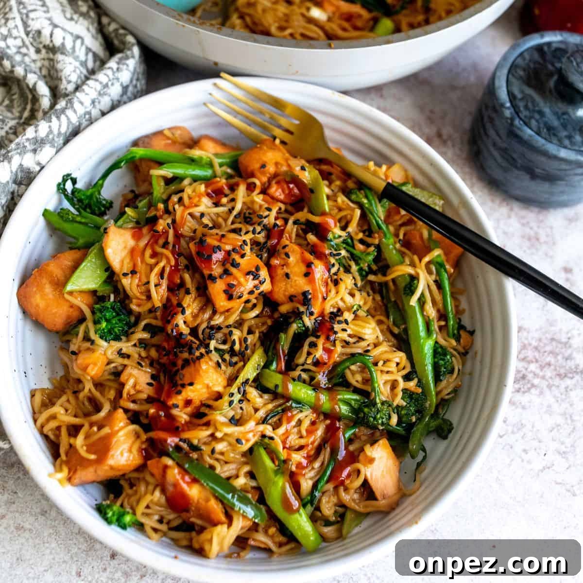 Teriyaki Salmon Noodles In a white bowl with black sesame seeds and a fork. 