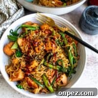 Teriyaki Salmon noodles in a white bowl with a black fork in the bowl.