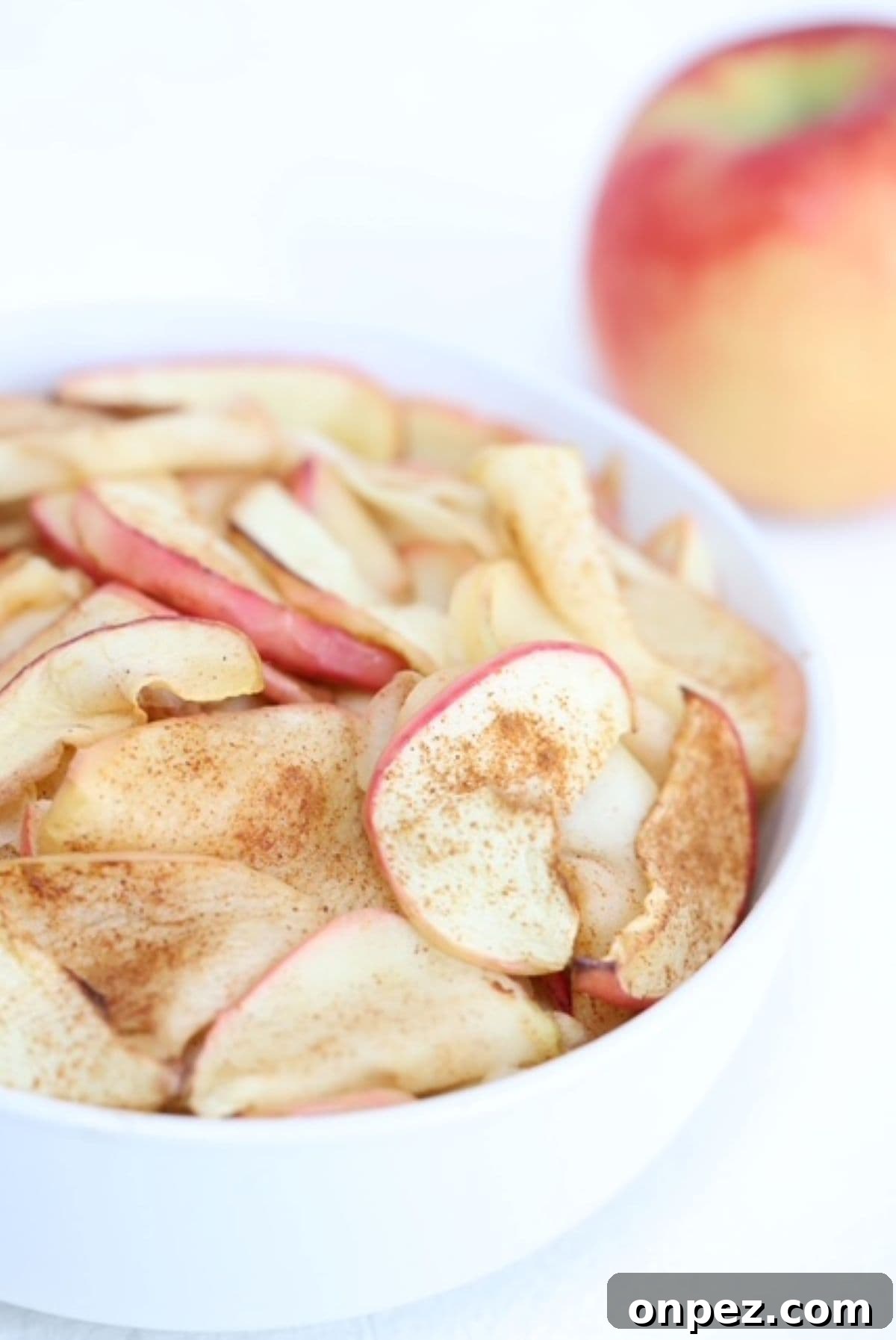 Air fried apple slices in a white serving bowl with an apple in the background.