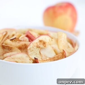Air fried apple slices in a white bowl with an apple in the background.