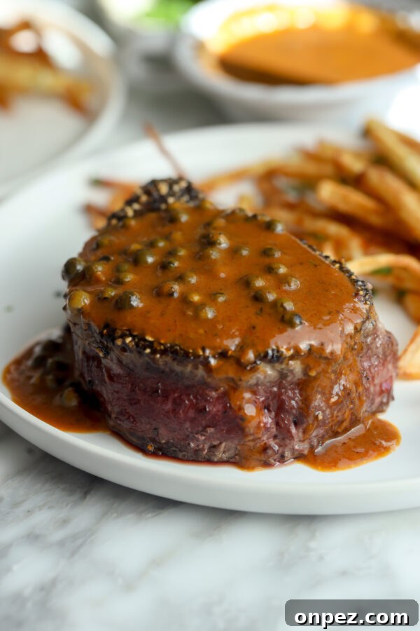 A tenderloin steak covered in peppercorn sauce with crispy fries in the background.