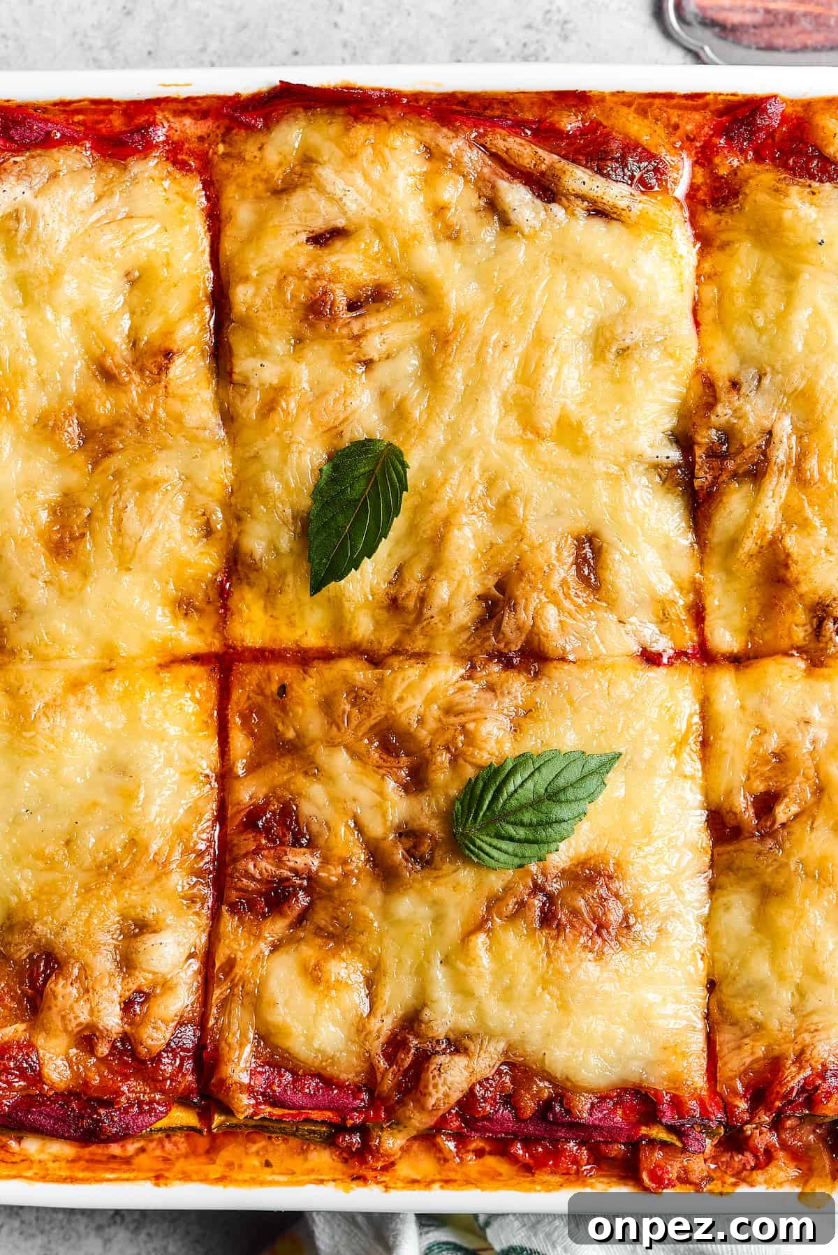 Close-up shot of a pan of baked lasagna, cut into large squares.