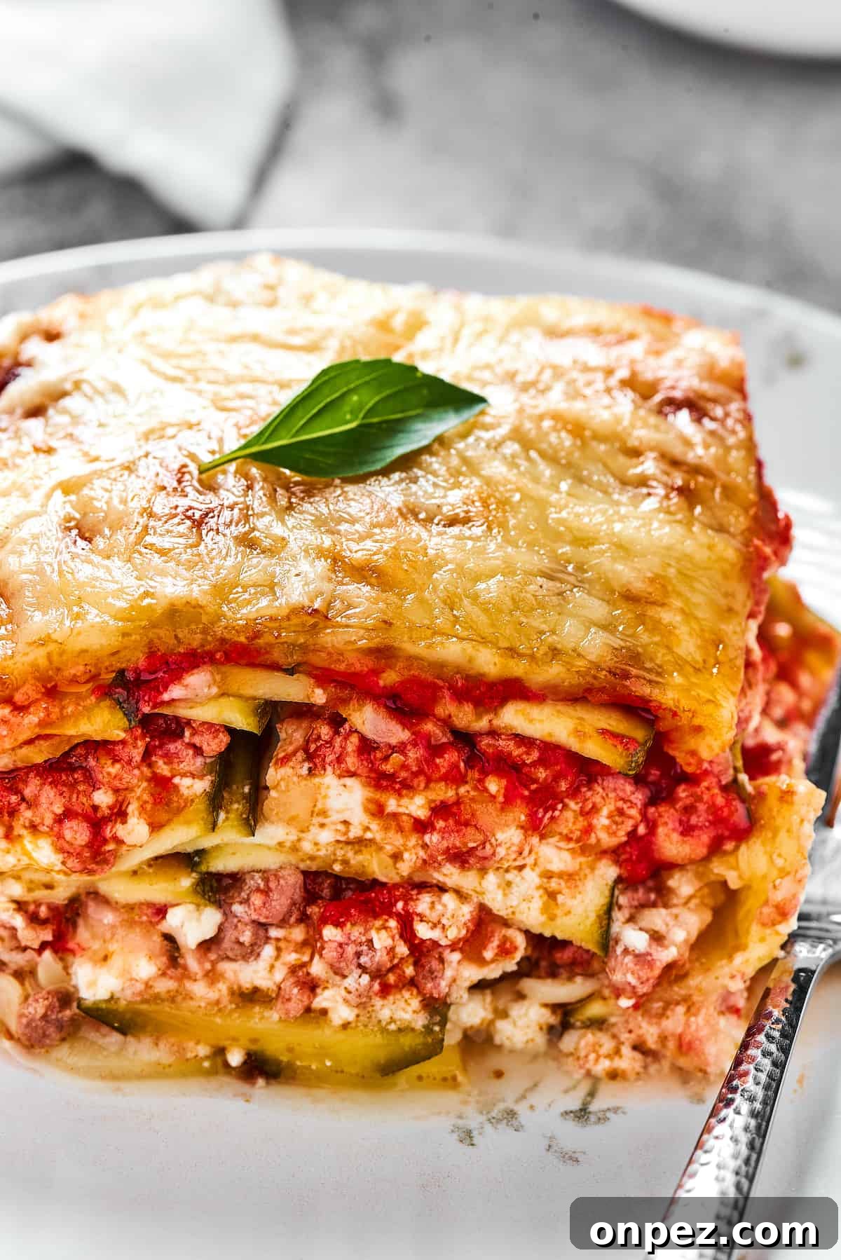 A serving of lasagna on a white plate with a fork.