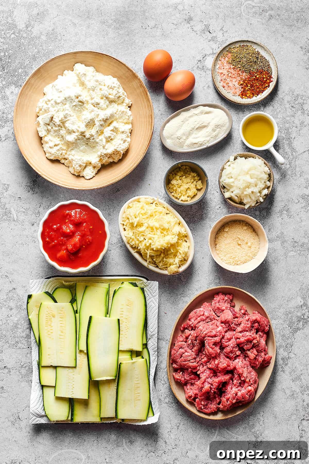From top left: Cottage cheese, eggs, seasonings, flour, olive oil, garlic, diced onion, crushed tomatoes, mozzarella, Parmesan, zucchini slices, ground beef.