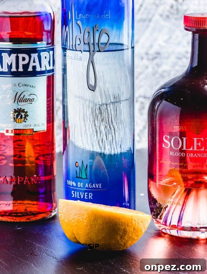 A bottle of Campari, bottle of tequila, bottle of Solerno blood orange liquor and half an orange.