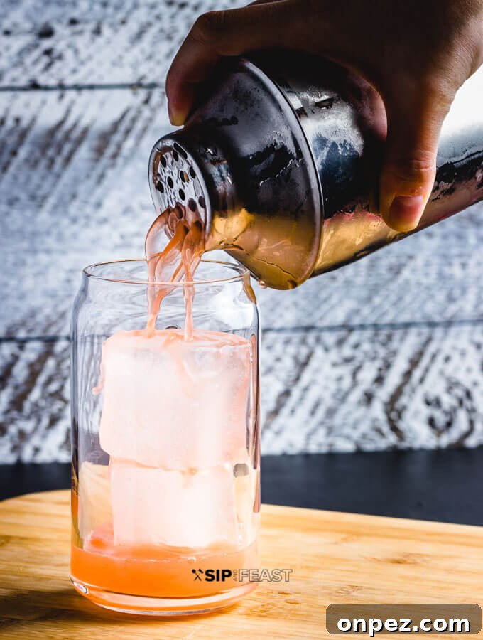 A glass of ice and a cocktail shaker pouring the Italian Margarita into the glass.