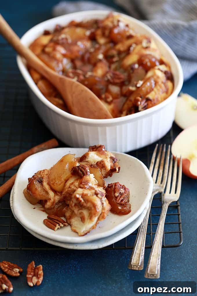 A serving of Apple Pie Biscuit Casserole on a white plate with forks and a casserole dish behind it.