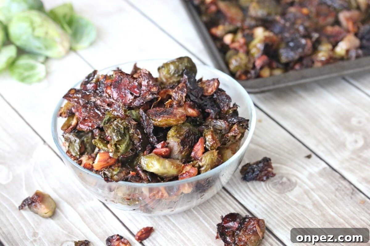 16 Maple Recipes for Deep, Caramel Sweetness 3 A clear bowl filled with roasted Brussels sprouts and pecans sits on a wooden surface, their caramelly sweetness shining through, with a baking tray of this maple-kissed mixture in the background.