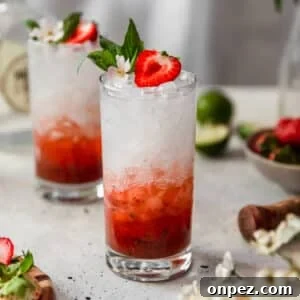 Two strawberry cocktails on a counter with a bowl of berries and a wooden muddler.