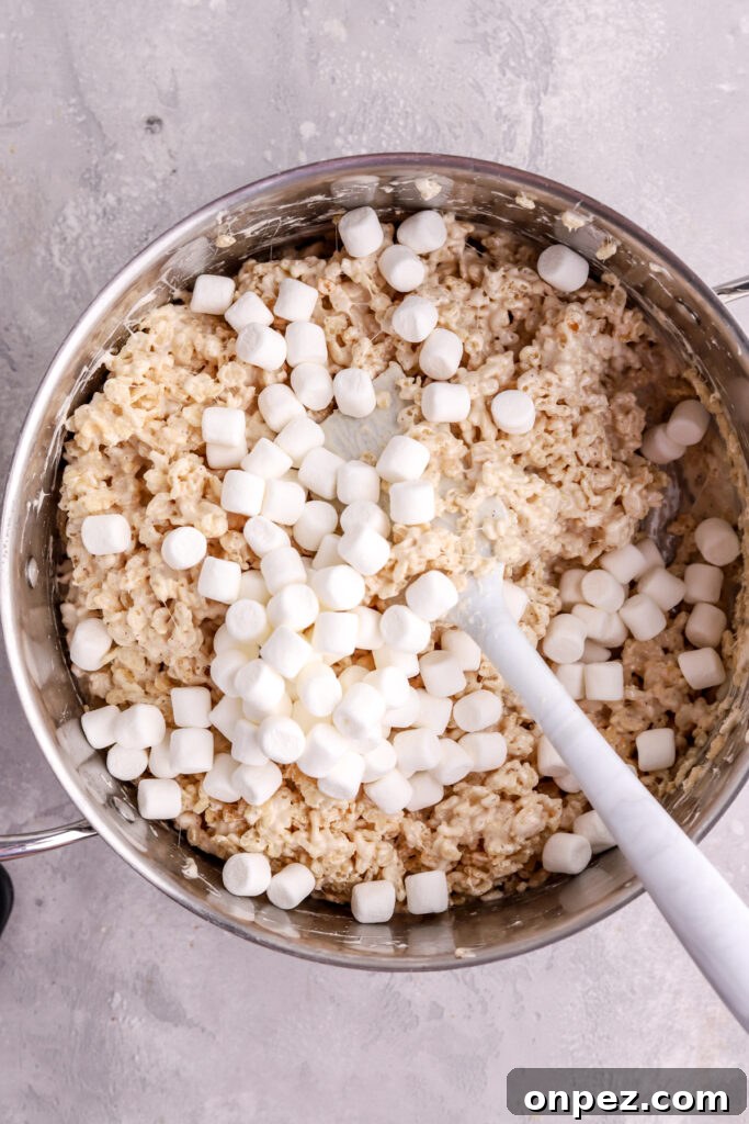 M&M Rice Krispie Treats Recipe 6 Rice Krispie treats in a pot with mini marshmallows and a spatula.