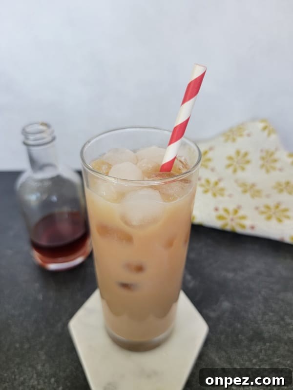 Iced Chai Tea Latte in a tall glass with a striped straw next to a bottle of chai concentrate