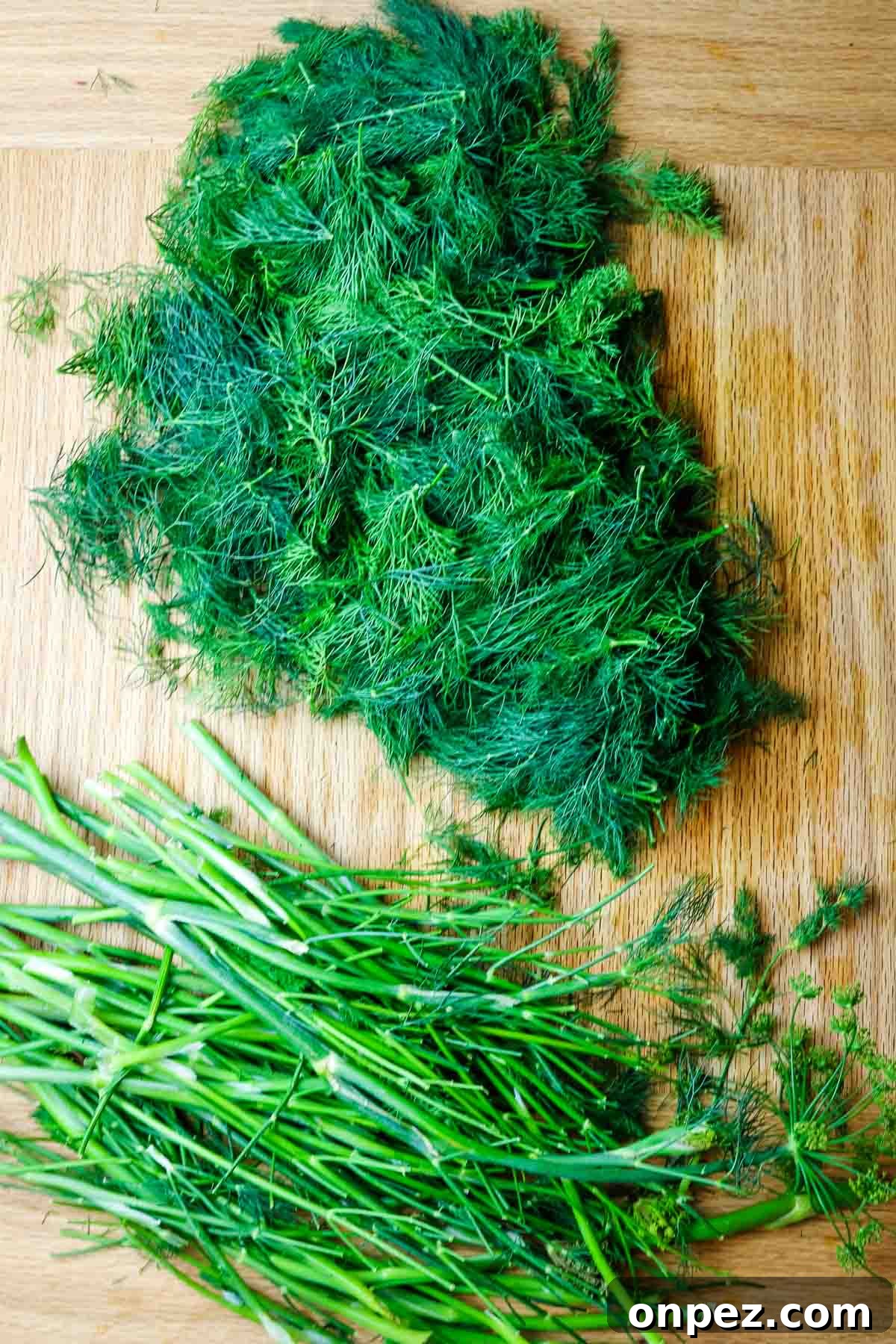 How to Chop Fresh Dill for Maximum Flavor and Yield 5 dill weed separated from dill stems on a wooden cutting board.