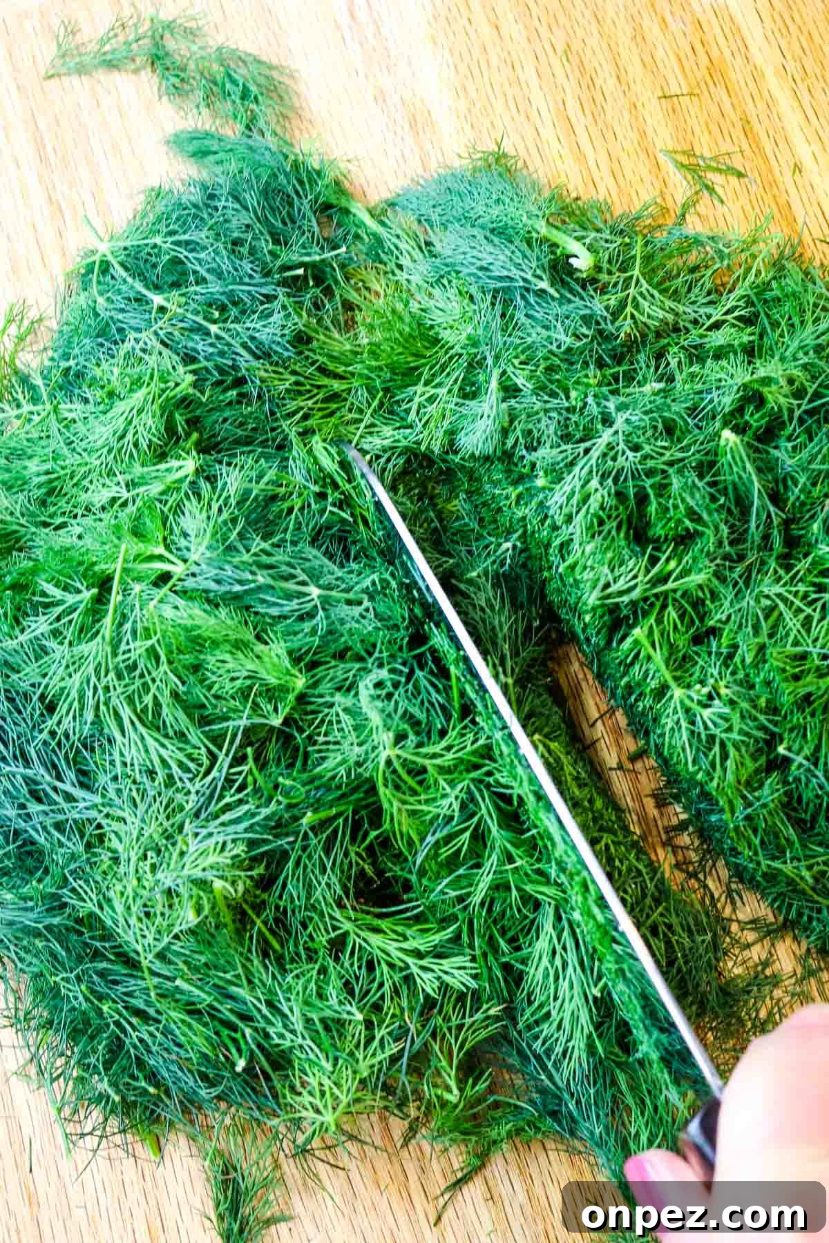 How to Chop Fresh Dill for Maximum Flavor and Yield 6 Feathery fresh dill weed chopped on a cutting board with knife to the side.