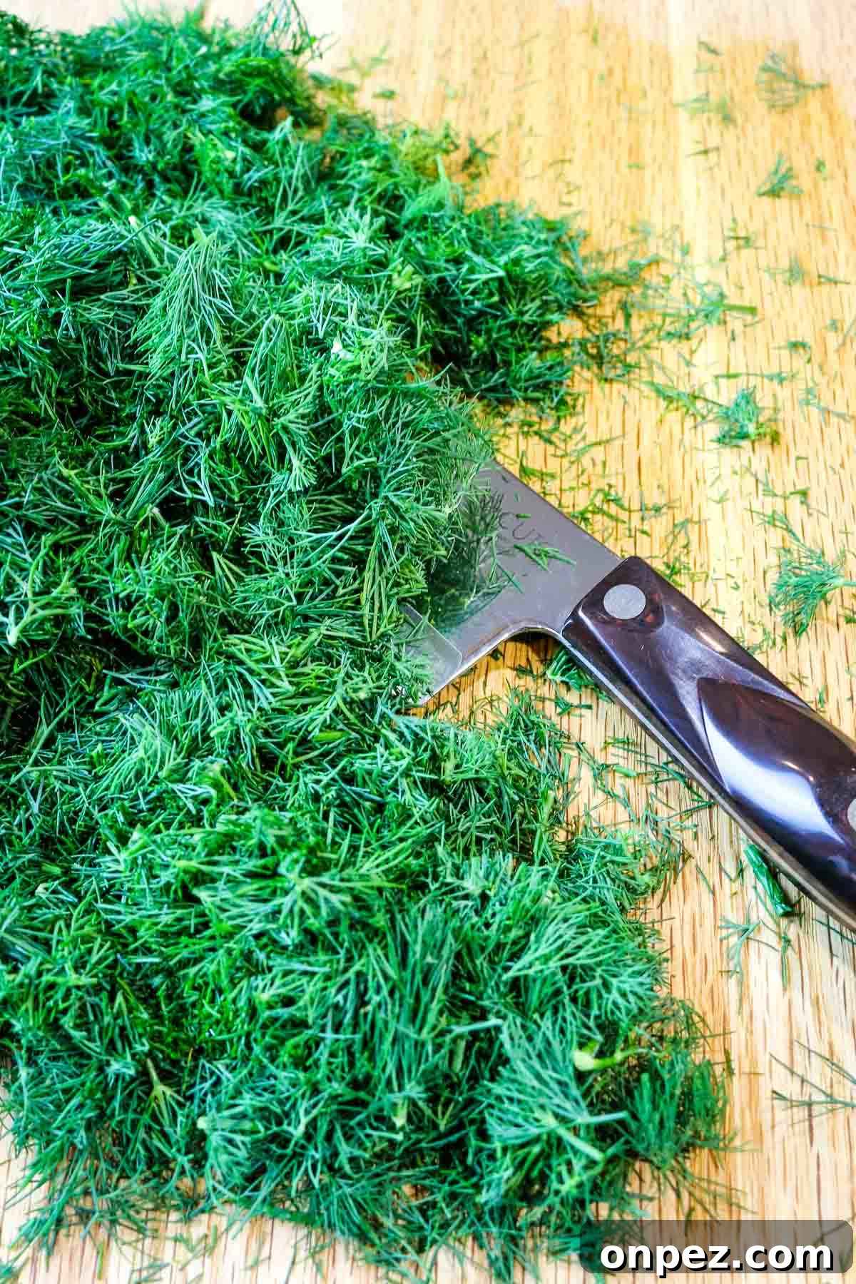 How to Chop Fresh Dill for Maximum Flavor and Yield 7 chopped fresh dill on a wooden board with knife to the side.