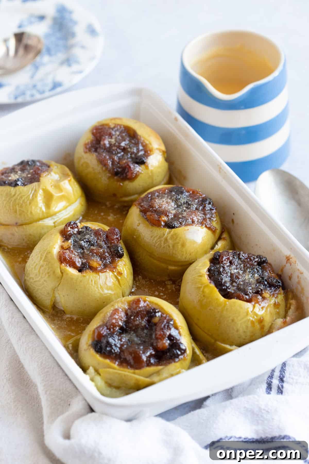 Baked apples in a white pie dish with a jug of custard.