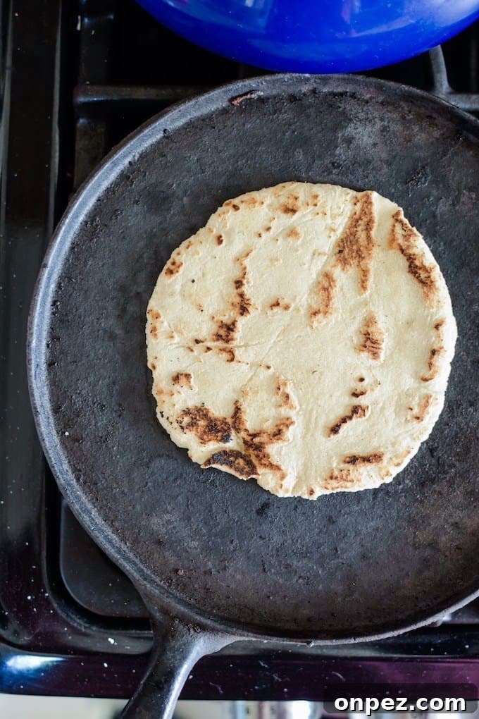 How to Make Authentic Corn Tortillas at Home 6 Overhead shot of a corn tortilla cooking in a black pan on the stove top.
