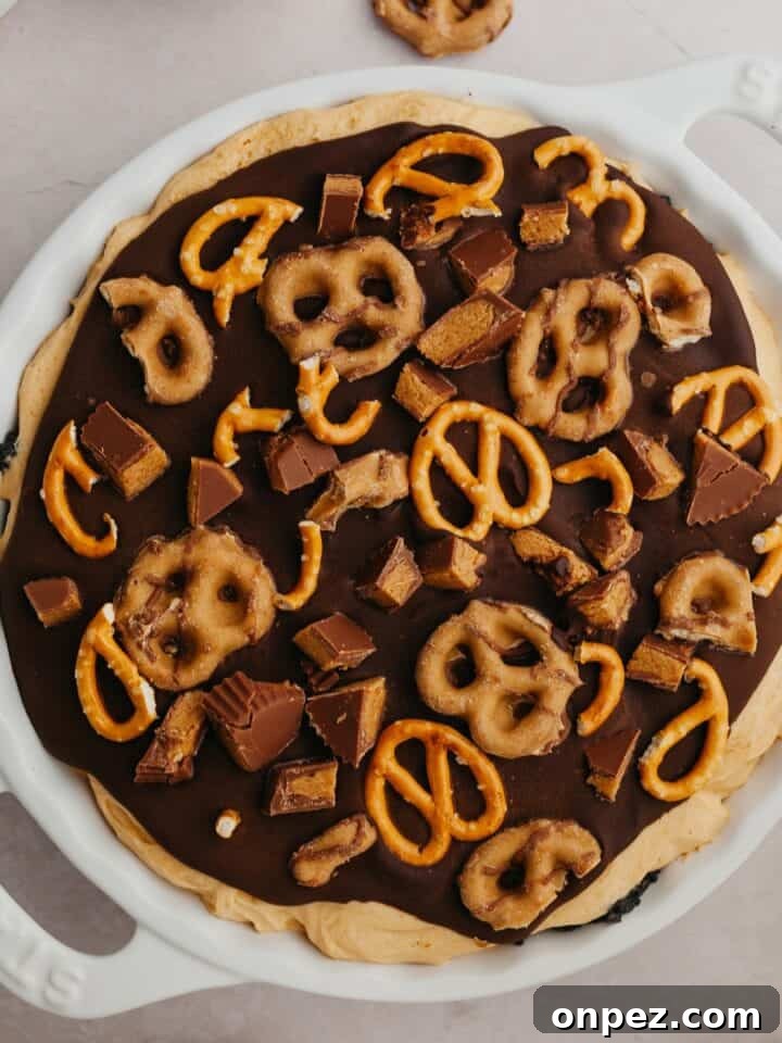 An overhead shot of a pie dish with a peanut butter pie covered in ganache and pretzels.