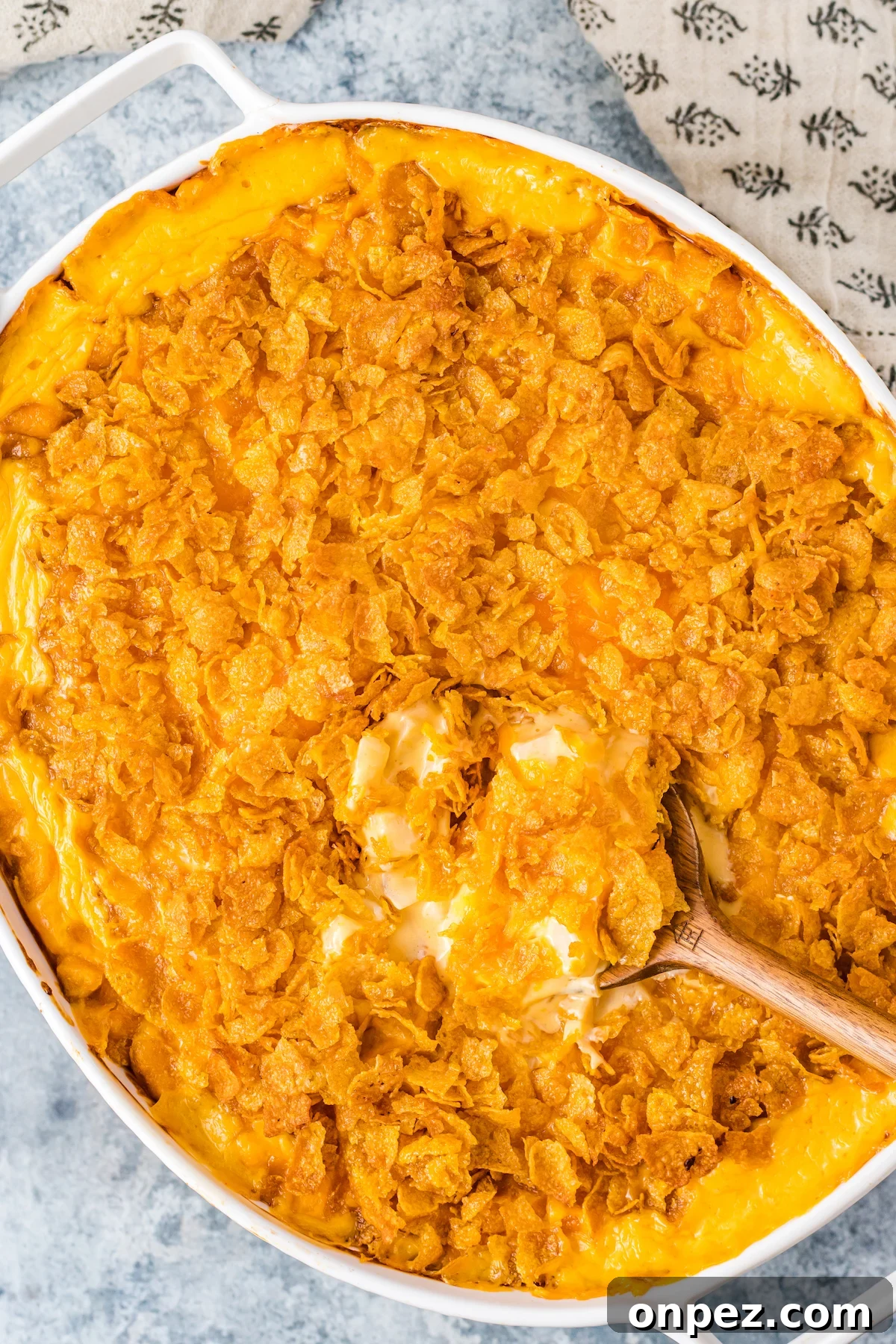 Classic Funeral Potatoes: Creamy Hashbrown Casserole Recipe 2 Overhead view of white oval baking dish filled with orange, cheesy funeral potatoes topped with cornflakes.