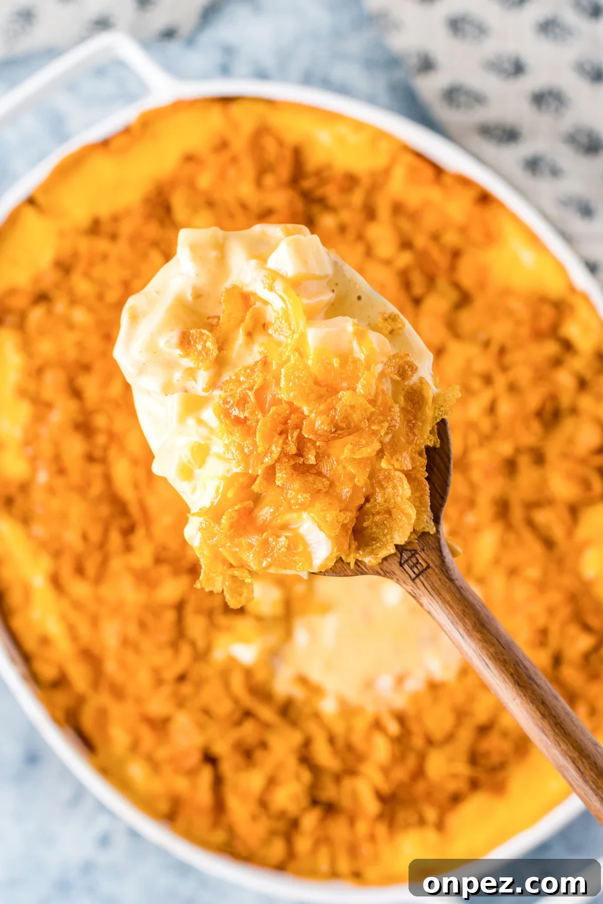 Classic Funeral Potatoes: Creamy Hashbrown Casserole Recipe 3 A wooden spoon is filled with funeral potatoes. The casserole dish is out of focus in the background.