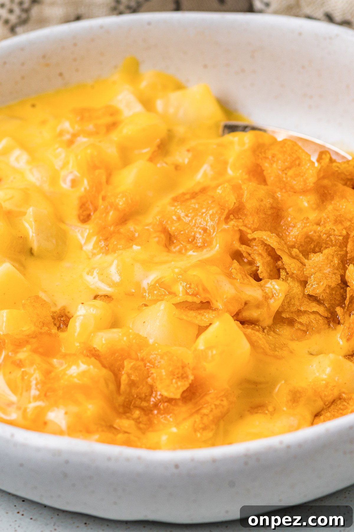 Classic Funeral Potatoes: Creamy Hashbrown Casserole Recipe 7 Close up of a serving of cheesy hash brown casserole in a white bowl.