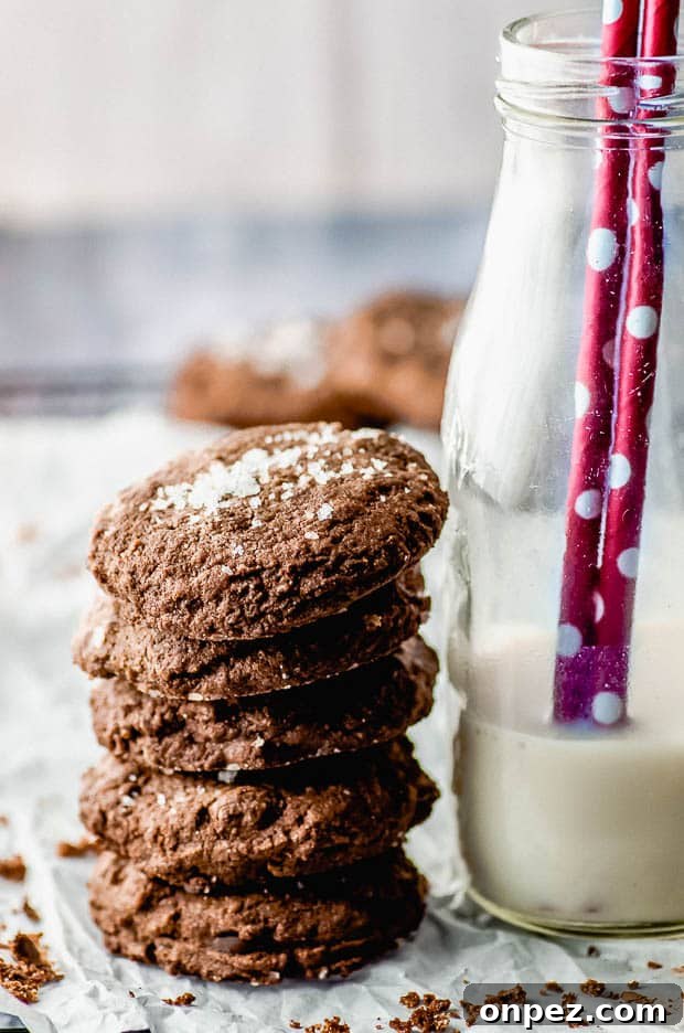 Side view of a pile of double chocolate chip cookies next to a bottle of milk
