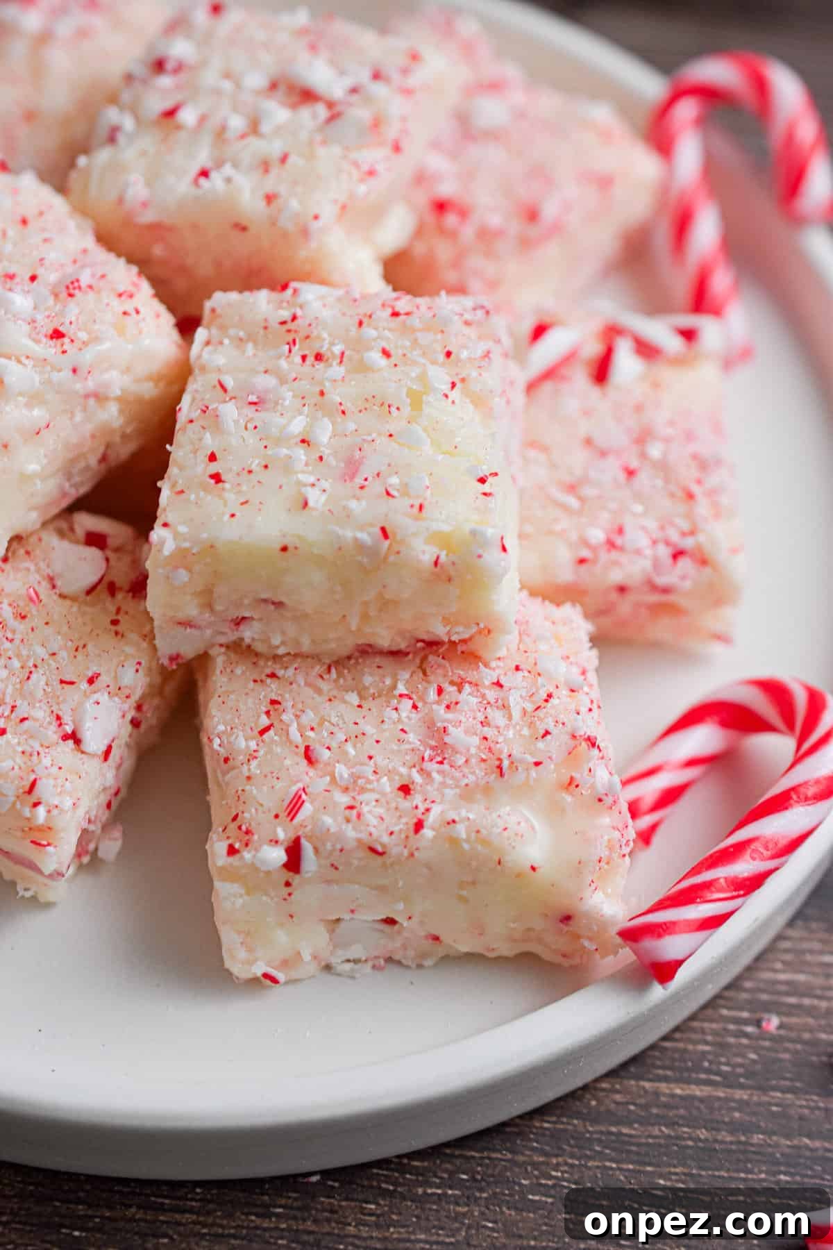 A pile of white chocolate peppermint fudge is on a white plate surrounded by small candy canes.